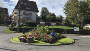 Un barrio residencial con un edificio de varios pisos, una glorieta con indicaciones y jardines bien cuidados.