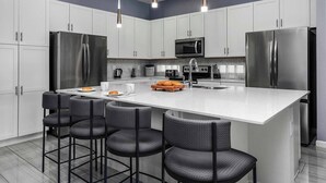 A modern kitchen with white cabinets, stainless steel appliances, and a central island with bar stools. - Grand Home w/ Princess & Wizard Themed BRs, Theater, Arcade & Pool - Near Parks (Davenport)