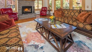 A spacious living room with a stone fireplace, leather sofas, and a large coffee table. - Charming Big Sky Condo! Cozy Fireplace, 10 Min Drive to Resort, 3 Min drive to T (Big Sky)