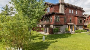 A two-story house with a stone chimney, large windows, and a balcony. - Charming Big Sky Condo! Cozy Fireplace, 10 Min Drive to Resort, 3 Min drive to T (Big Sky)