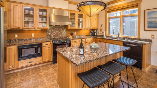 A spacious kitchen with wooden cabinets, granite countertops, a built-in oven, and a large island with bar stools. - Charming Big Sky Condo! Cozy Fireplace, 10 Min Drive to Resort, 3 Min drive to T (Big Sky)