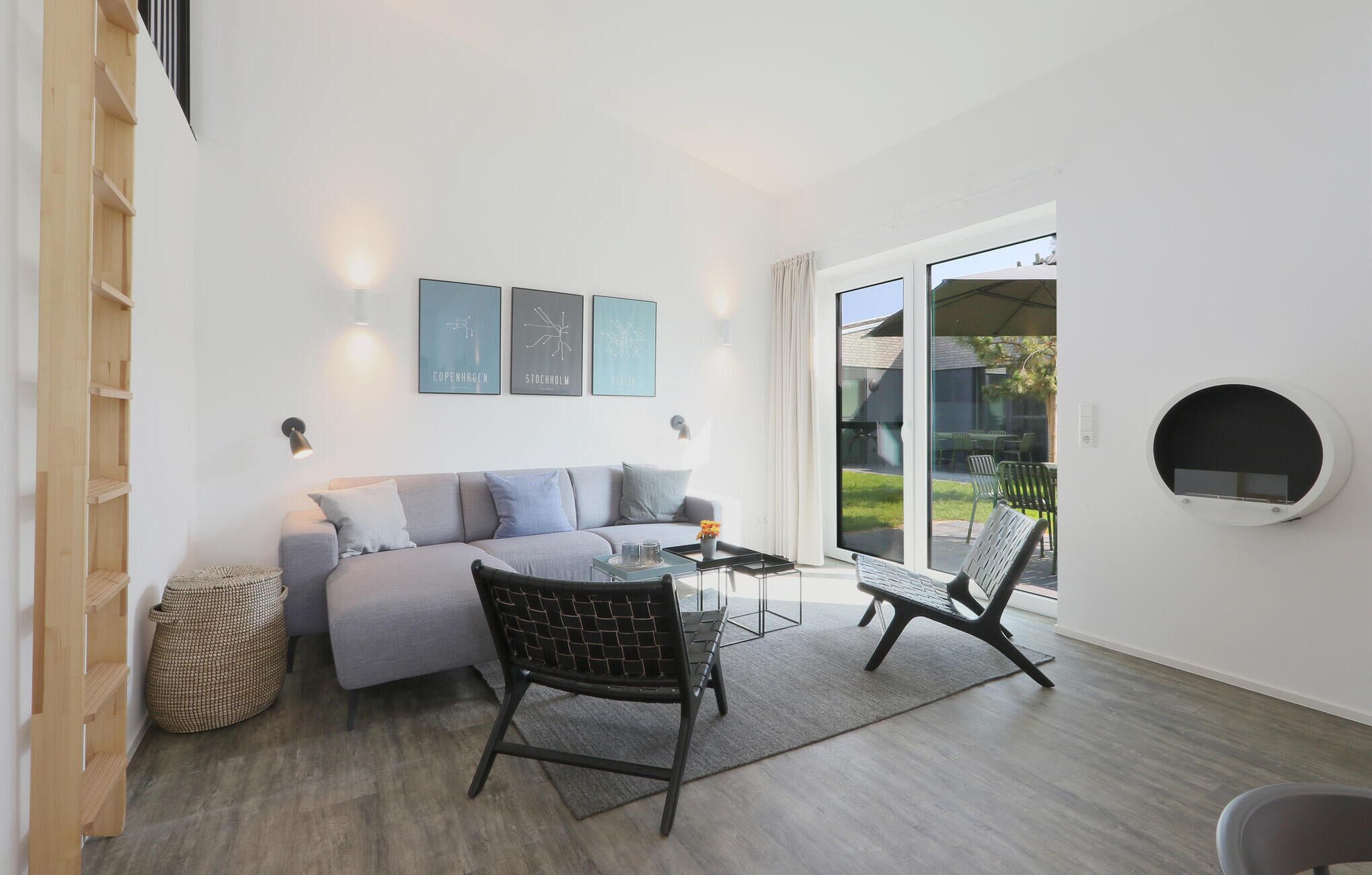 A modern living room with a grey sofa, two black chairs, a coffee table, and a large window with a view of the outdoors.