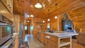 Interior de una cabaña de madera con cocina, que incluye una isla grande, armarios de madera e iluminación colgante.