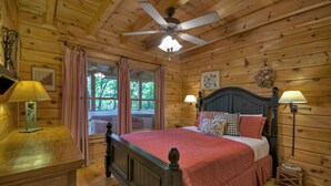 A wooden cabin bedroom with a bed, two bedside lamps, a ceiling fan, and a window with curtains. - Pate`s Escape - Cherry Log (Cherry Log)