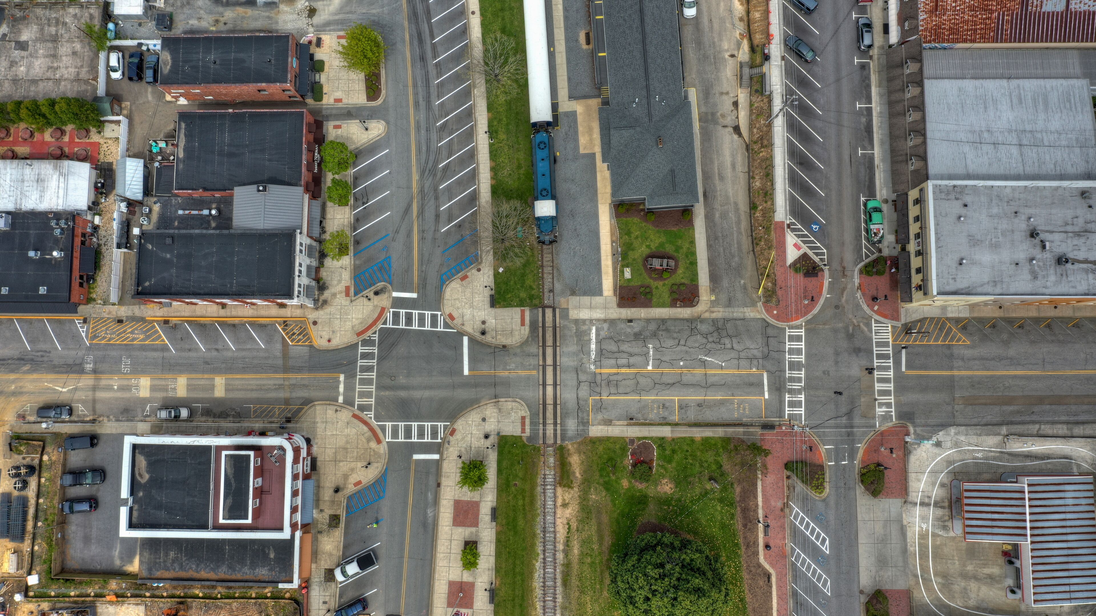 An aerial view of a city intersection with multiple lanes, parking spaces, and buildings.