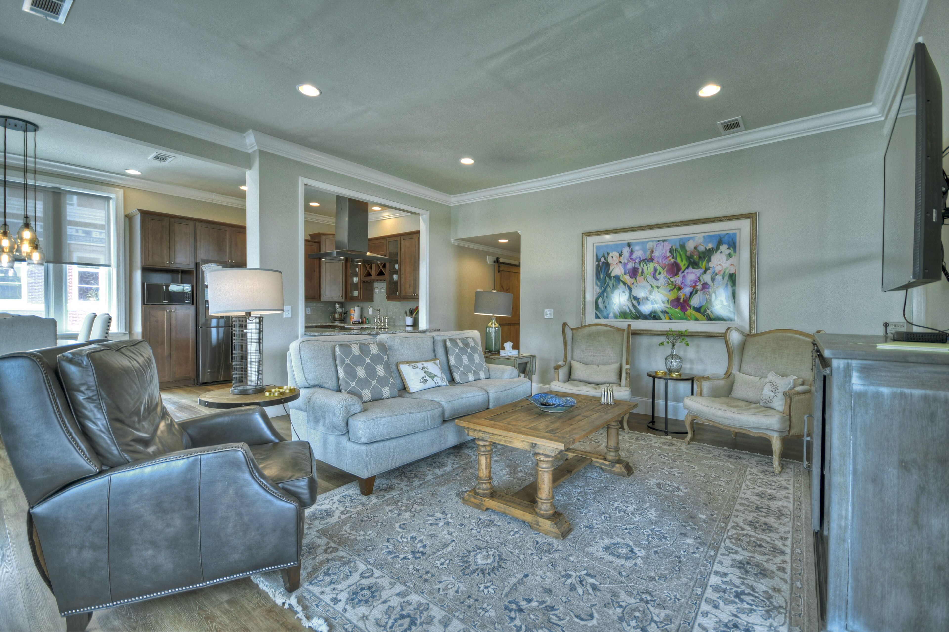 A spacious living room with a grey sofa, leather armchairs, a wooden coffee table, and a patterned rug.