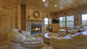A cozy cabin interior with a stone fireplace, leather couches, and a television.