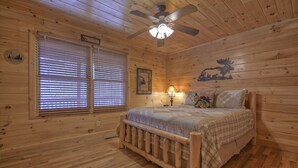 A wooden cabin bedroom with a bed, a ceiling fan, and a window with blinds.