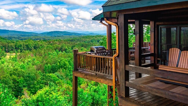 Une terrasse en bois avec un barbecue et des chaises, donnant sur un paysage boisé.