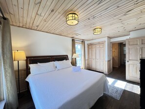 Een slaapkamer met een groot bed, houten plafond en twee bedlampjes.