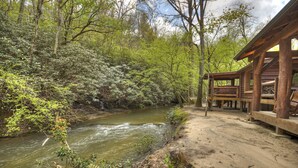 Eine rustikale Holzhütte mit einer Holzterrasse, die auf einen Fluss mit Blick auf dicht bewachsenen Wald blickt.