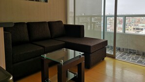 A modern living room with a sectional sofa, a glass coffee table, and a large window offering a city view. - LIMA FLAT 8 1D BETWEEN AIRPORT AND MIRAFLORES (Cercado de Lima)