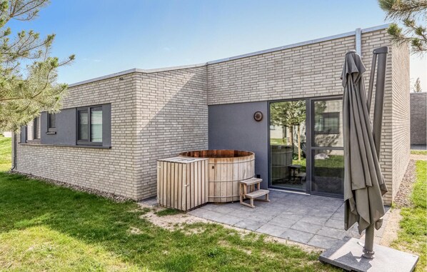 A modern house with a brick exterior, a wooden hot tub, and a patio area with a table and chairs.