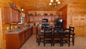 Cocina de estilo cabaña de madera con comedor, que incluye armarios de madera, encimera de granito, microondas, refrigerador y una araña.