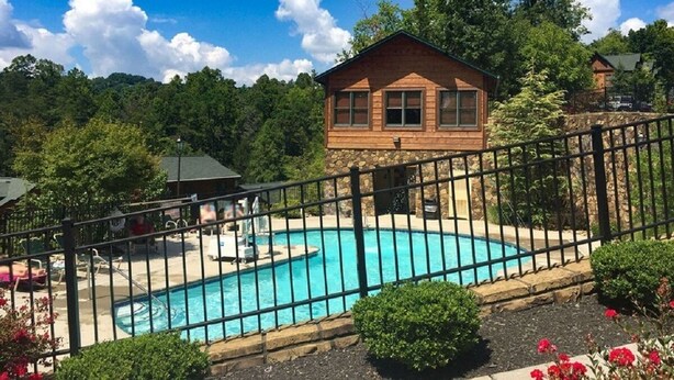 Una cabaña de madera con piscina, rodeada por un muro de piedra y una valla de metal.