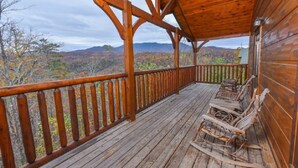 Una terraza de madera con barandilla, sillas de madera rústica y vistas a follaje otoñal y montañas.