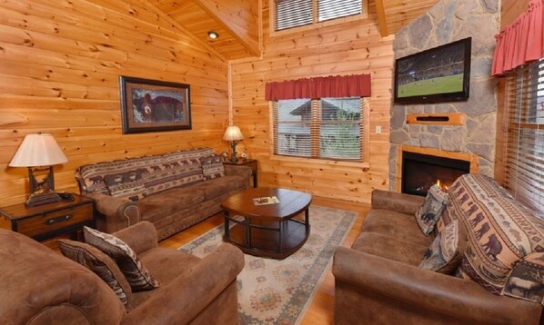 A cozy log cabin interior with a fireplace, wooden walls, a sofa set, and a television.