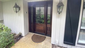 A house entrance with a wooden door, a doormat, and two wall-mounted lanterns.