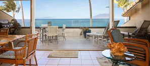 Enjoy ocean views and a distant mountain range from this balcony, featuring wicker chairs and a grill for outdoor dining.