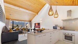 Eine moderne Küche mit weißen Schränken, einem eingebauten Backofen und einer großen Kochinsel mit Obstschale und Weingläsern.