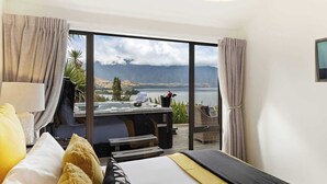 Ein Schlafzimmer mit großem Fenster, einem Bett, einer Whirlwanne und Blick auf einen See und Berge.