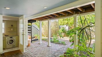 Un patio techado con lavadora, una escalera en espiral y un jardín con macetas.