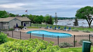 A swimming pool with lounge chairs and a view of a marina. - Best views on MDI - 2 bedroom 2 bath condo - waterfront with in ground pool (Southwest Harbor)