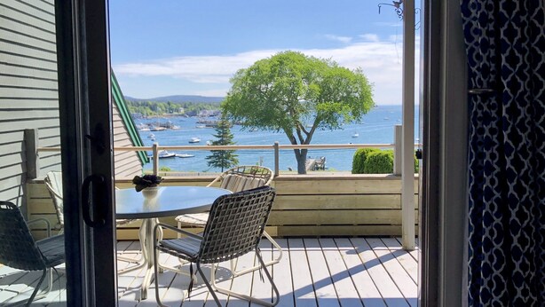 A wooden deck with a table and chairs, overlooking a body of water with boats and a tree. - Best views on MDI - 2 bedroom 2 bath condo - waterfront with in ground pool (Southwest Harbor)
