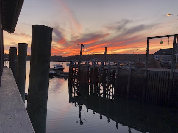 A waterfront dock with boats, a wooden pier, and a sunset in the background.