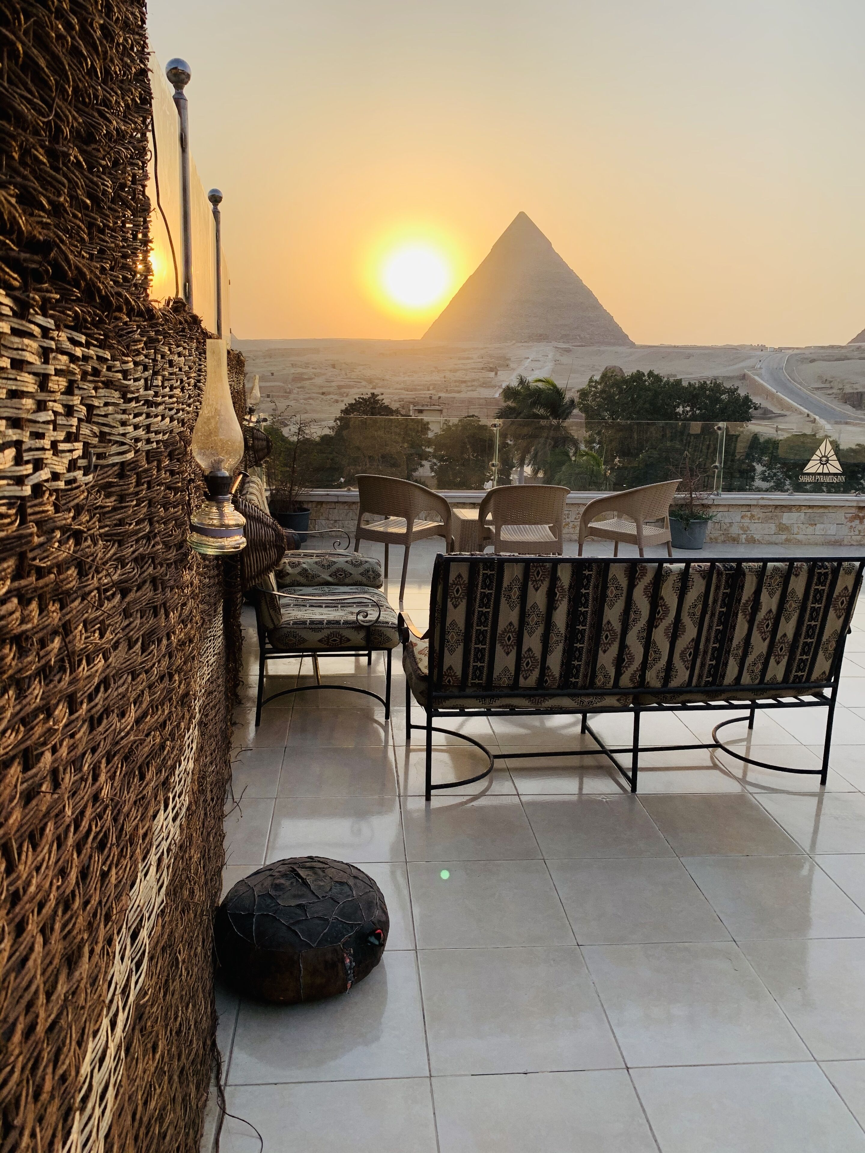 Eine Terrasse mit Korbmöbeln, einer Lampe und Blick auf die Pyramide im Sonnenuntergang.