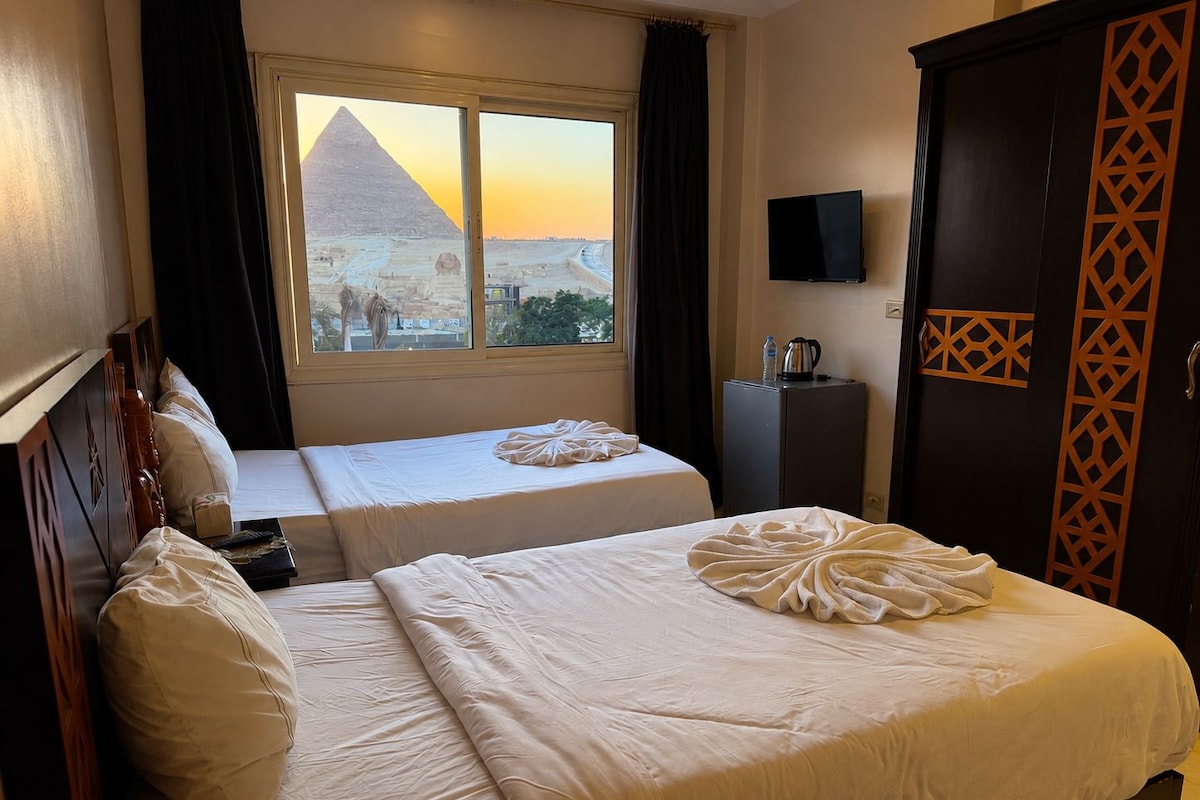 Quarto de hotel com duas camas, vista para as pirâmides, televisão de tela plana e minibar.