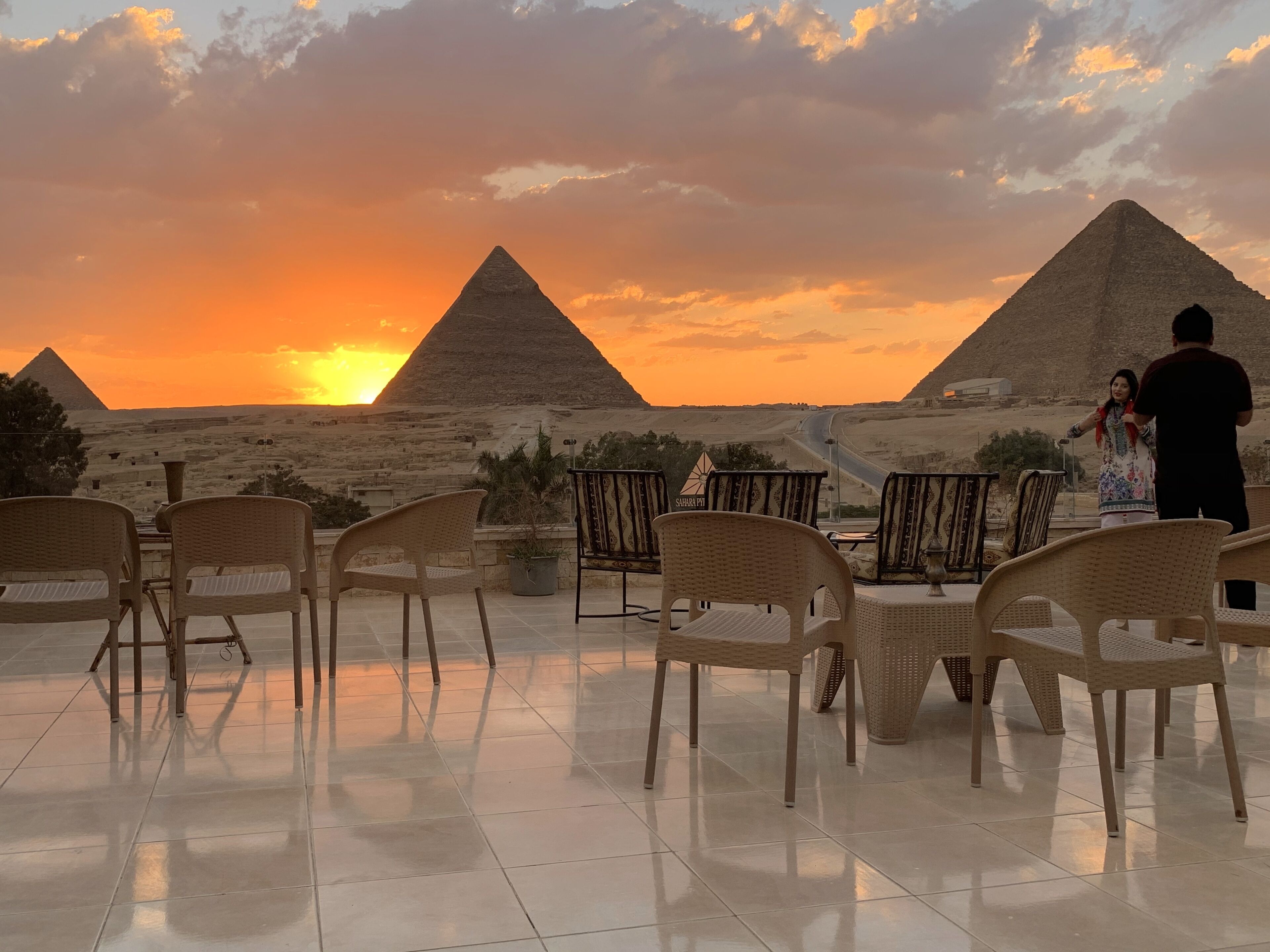 Una terraza con sillas de mimbre y vista a las pirámides al atardecer.
