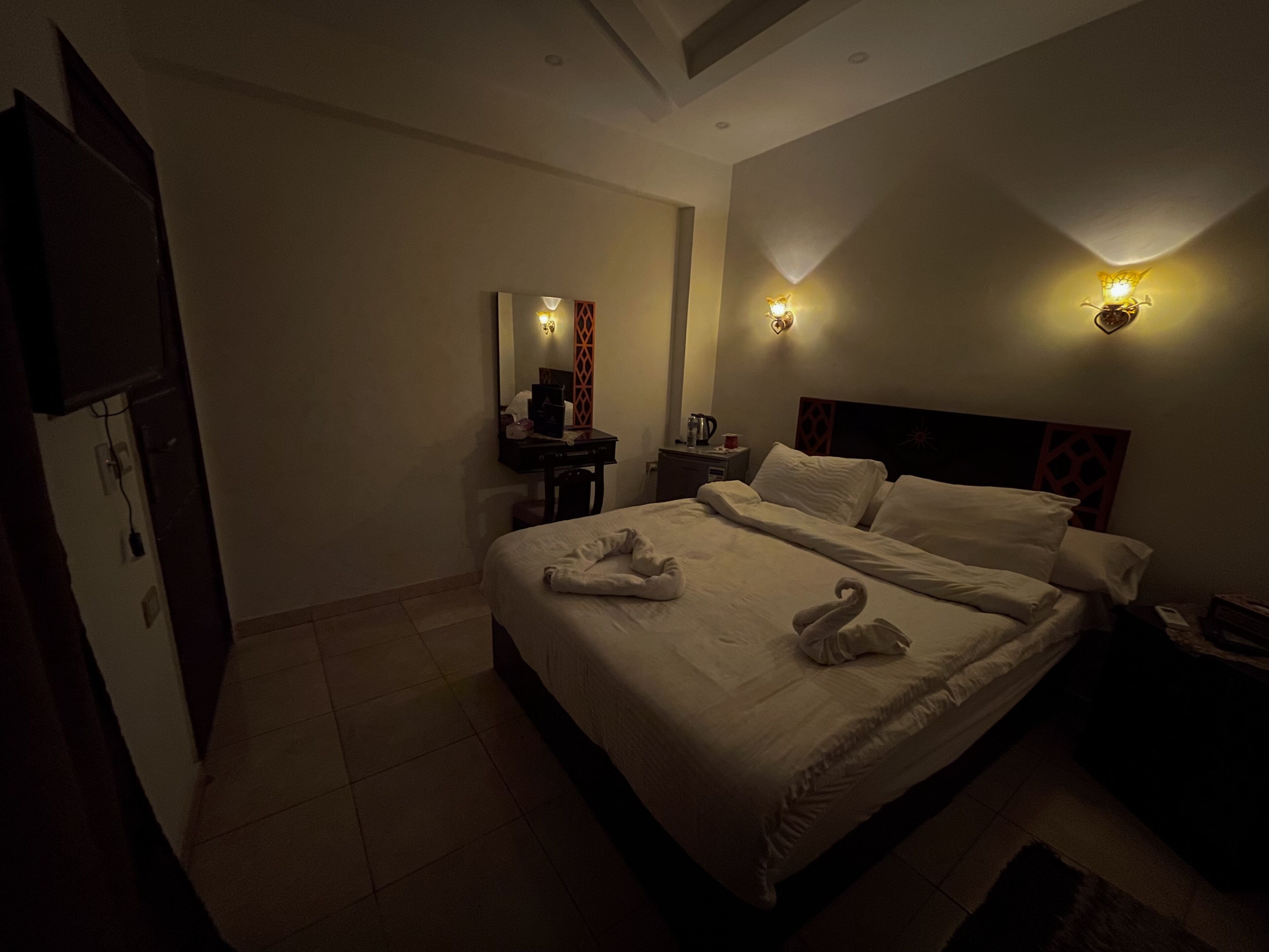 A hotel room with a bed, bedside tables, a mirror, and wall-mounted lights.