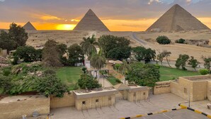 A view of the pyramids at sunset with a parking area and greenery in the foreground. - Sahara Pyramids Inn (Giza)
