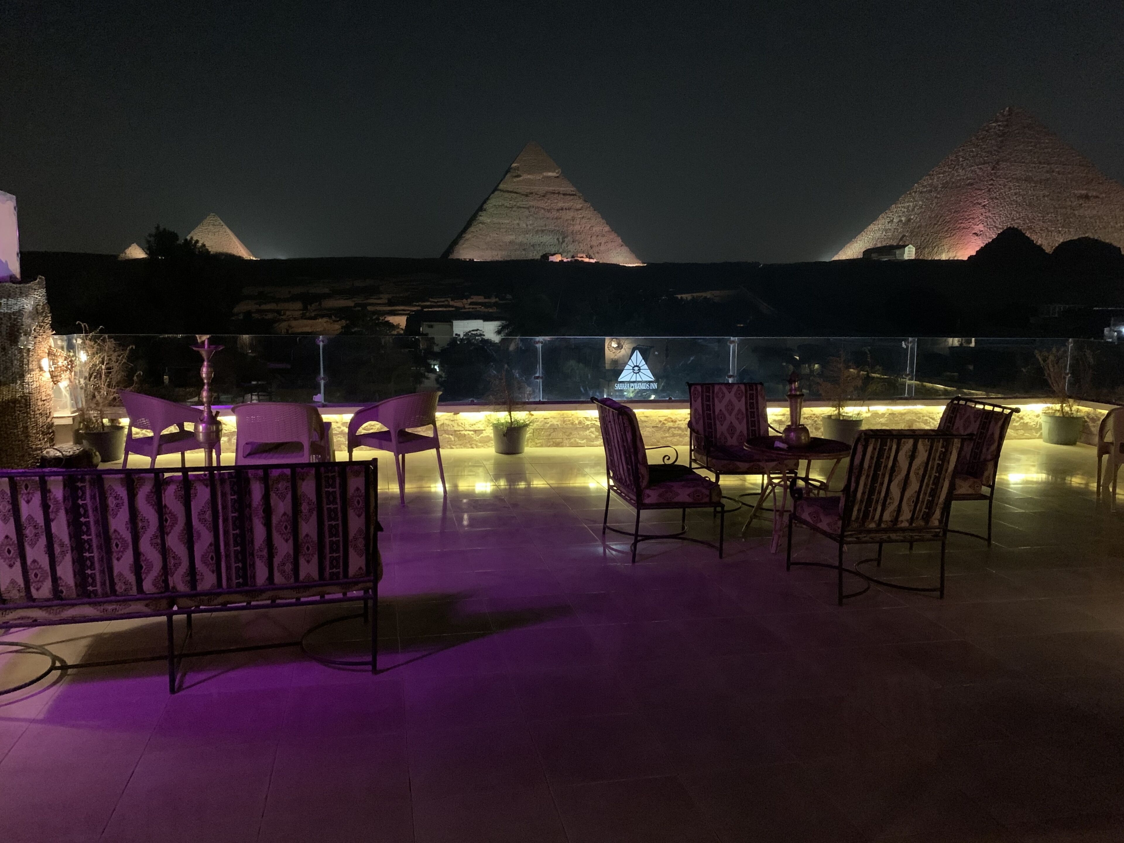 An outdoor seating area with chairs and tables, a view of the pyramids, and a sign for "Sphinx Dreams Inn".