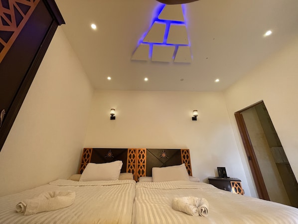 A hotel room with a large bed, two bedside tables, a nightstand, and a ceiling light fixture.