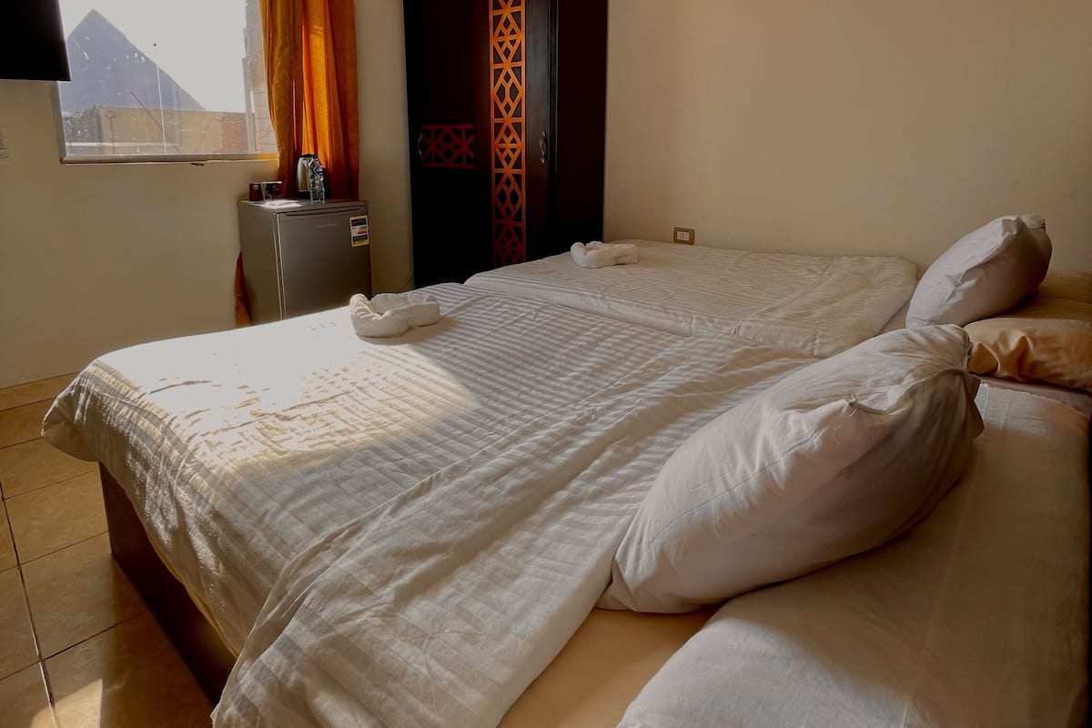 A bedroom with a large bed, a wardrobe, a small table with a kettle, and a window with curtains.