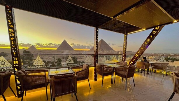 A terrace with wicker furniture and a view of the pyramids at sunset. - Sahara Pyramids Inn (Giza)