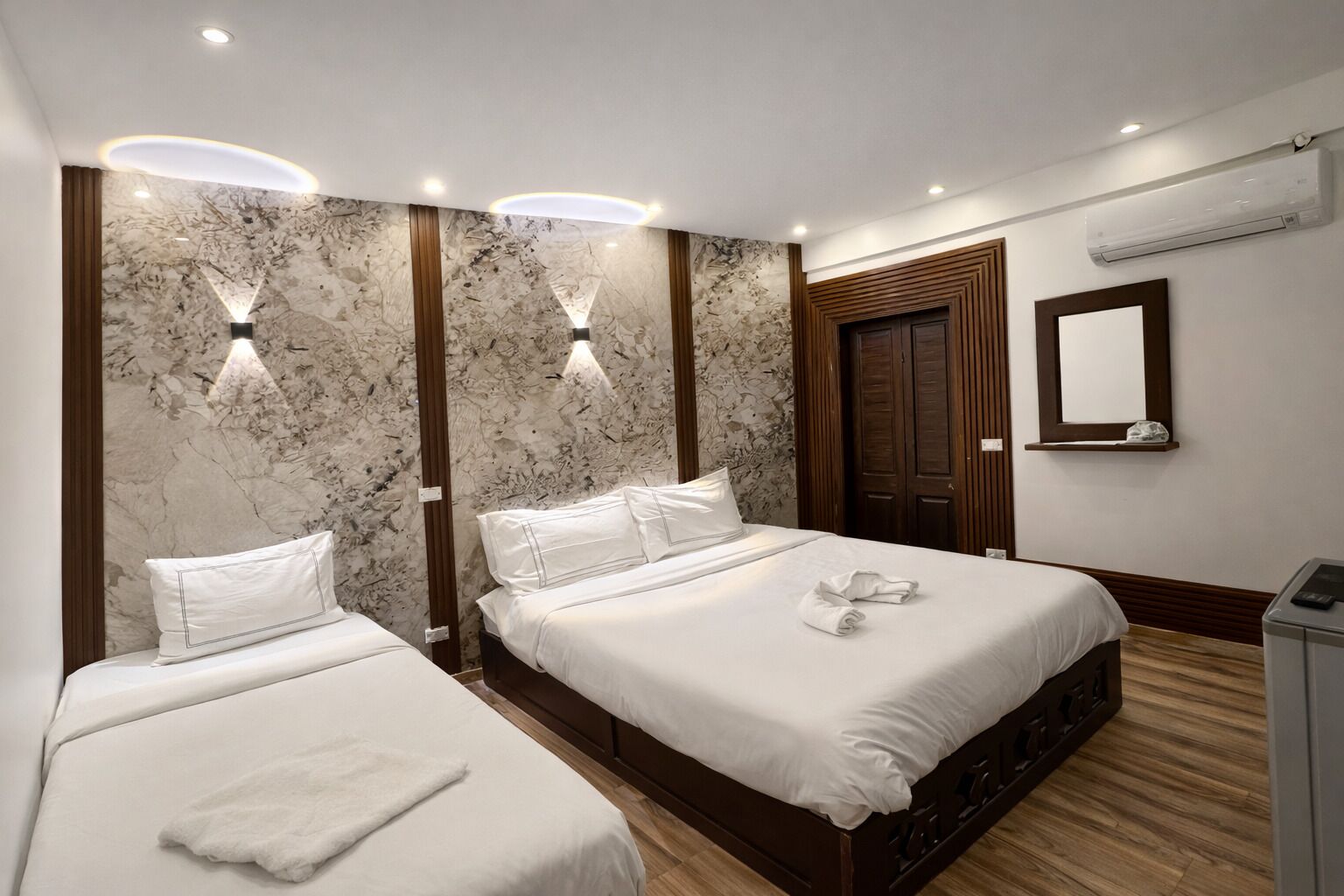 A modern hotel room with two beds, marble-patterned walls, wooden paneling, and a built-in air conditioning unit.