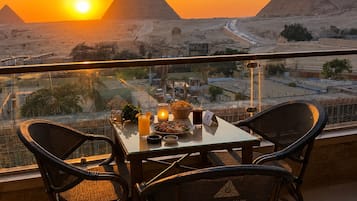 Una mesa de comedor con sillas en un balcón con vista a las pirámides al atardecer.