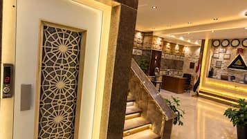 Eine Hotelhalle mit einer Rezeption, einer Treppe und einer Wand mit gerahmten Bildern.