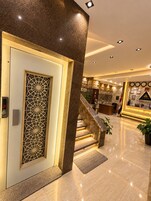 A hotel lobby with a reception desk, a staircase, and a decorative wall with framed pictures.