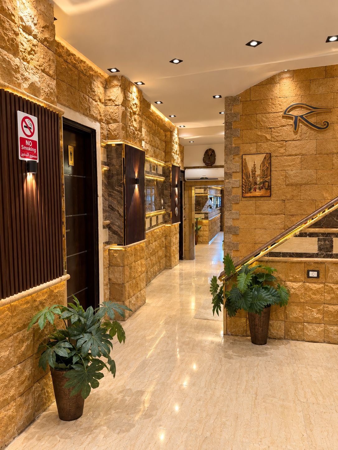 A hotel lobby with a stone wall, a no-smoking sign, a staircase, and potted plants.