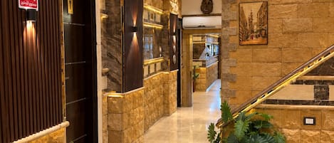 A hotel lobby with a stone wall, a no-smoking sign, a staircase, and potted plants.