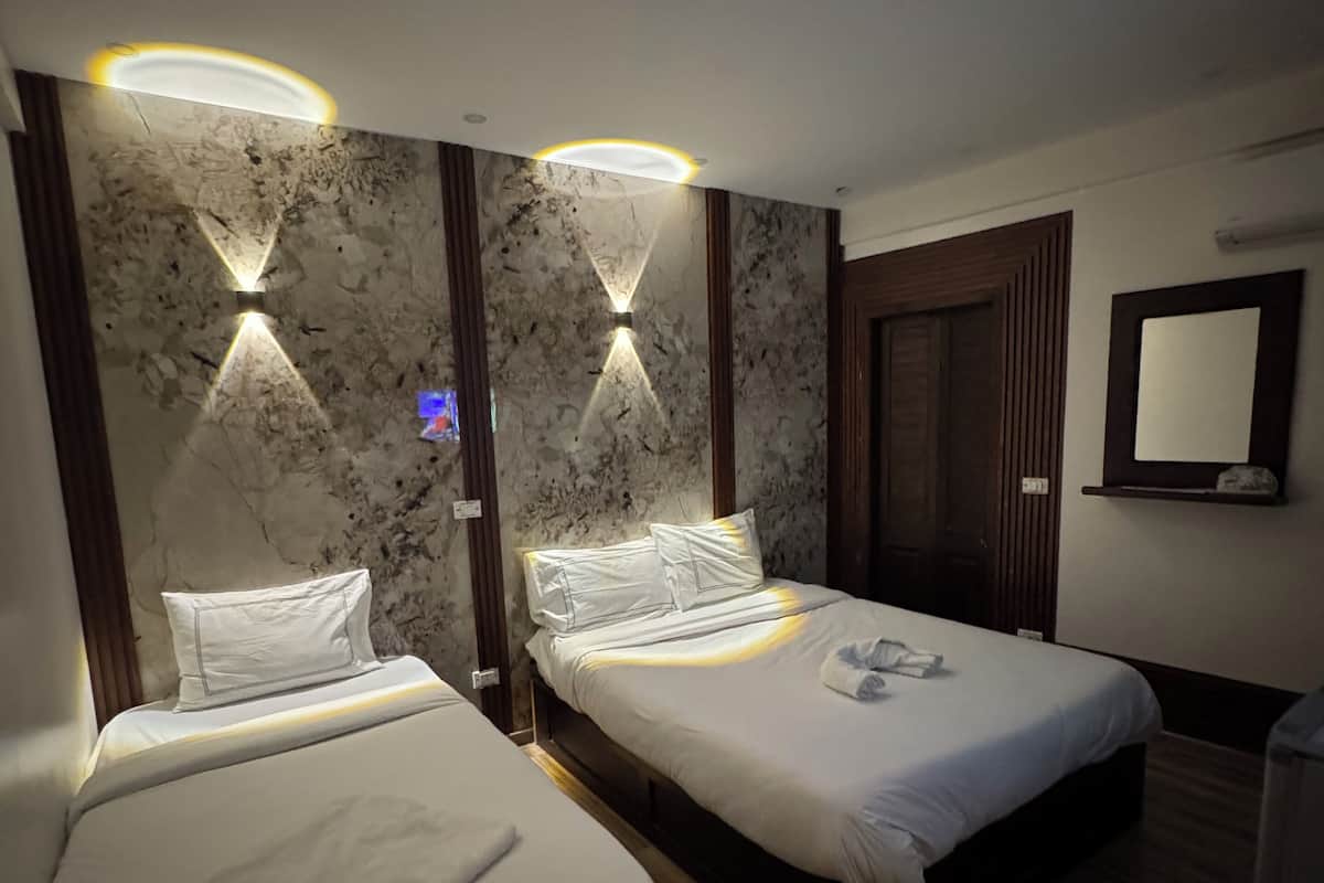 A hotel room with two single beds, marble-patterned walls, and built-in lighting.