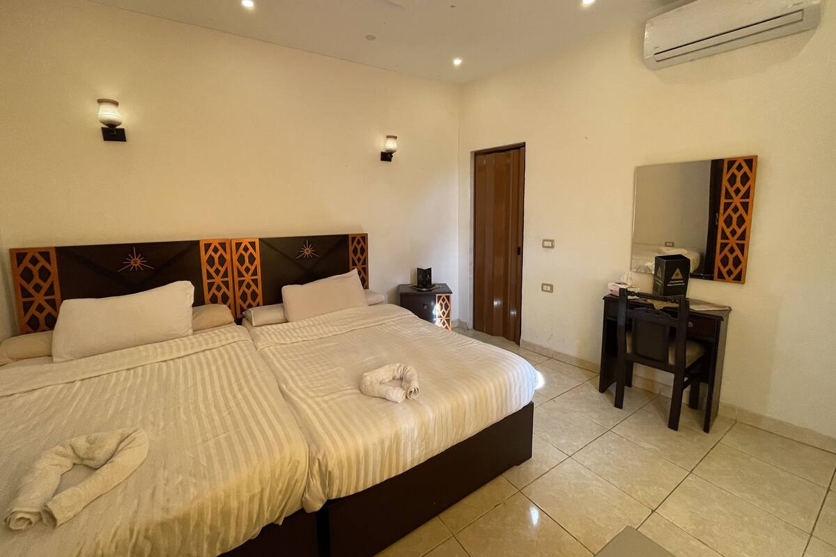 A hotel room with a large bed, a desk, a mirror, and an air conditioning unit.