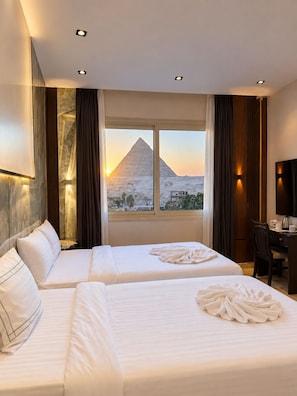 A hotel room with two beds, a desk, and a view of the pyramid at sunset. - Sahara Pyramids Inn (Giza)