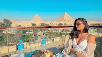 A table with food and drinks, a woman, and a view of pyramids.