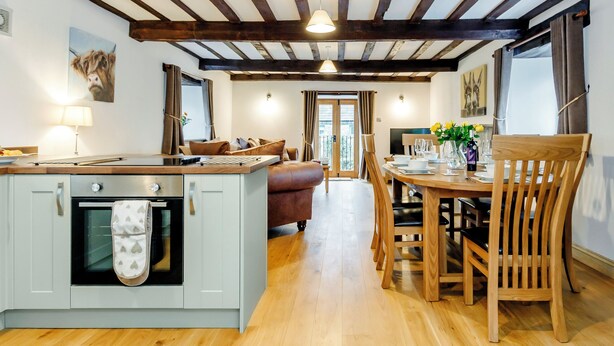 A kitchen with a built-in oven and a dining area with wooden furniture. - The Old Granary - UK12135 (Hewelsfield, near Lydney)
