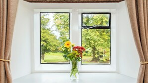 A window with a view of a tree and grass, a vase with flowers, and a wooden beam above. - The Old Granary - UK12135 (Hewelsfield, near Lydney)